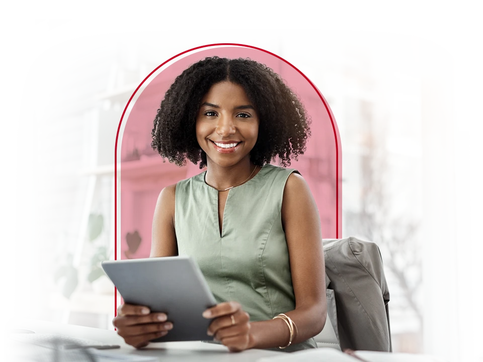 A woman sitting at a desk, smiling while holding a tablet.