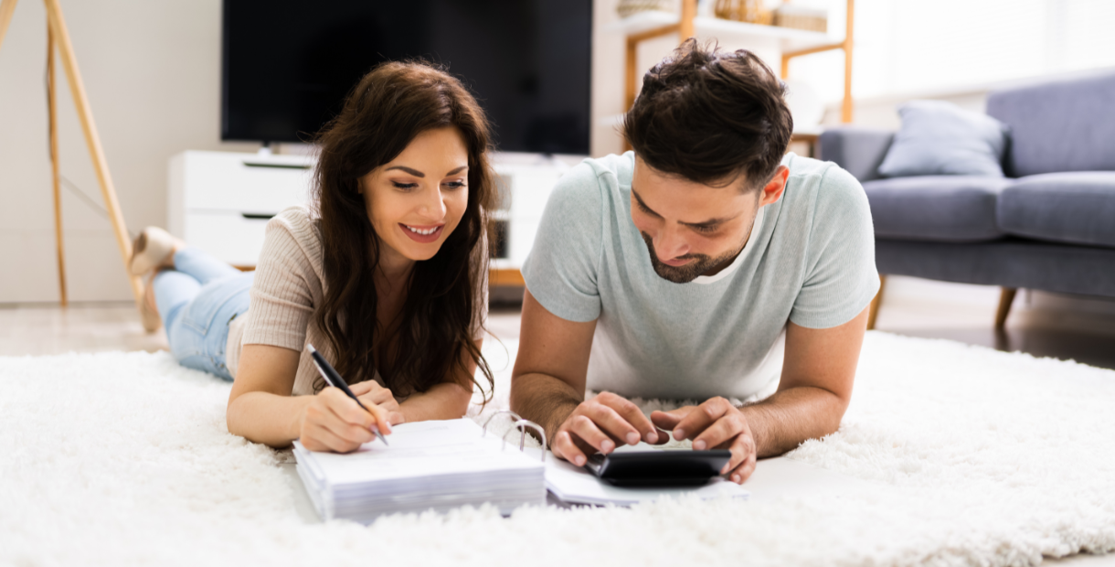 A couple lying on the floor with a calculator and binder. 