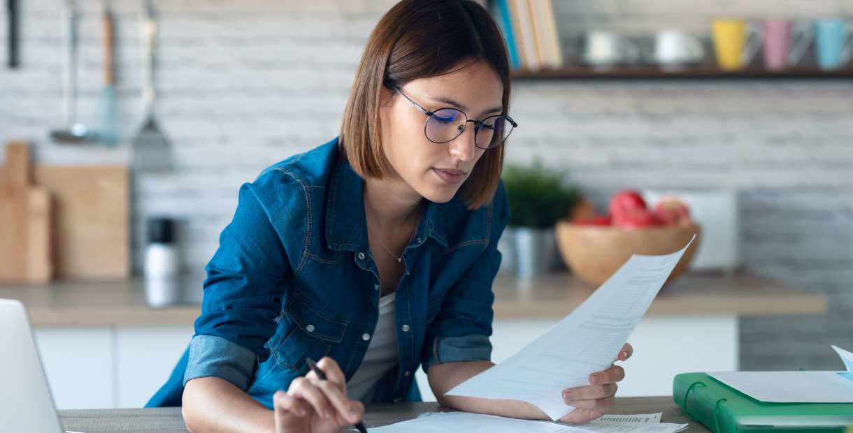 Woman looking at paperwork in her kitchen.