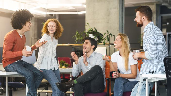 A group of diverse employees happily talking in a breakroom type space.