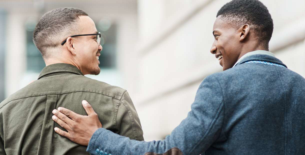 Two friends walking and talking in front of a building.