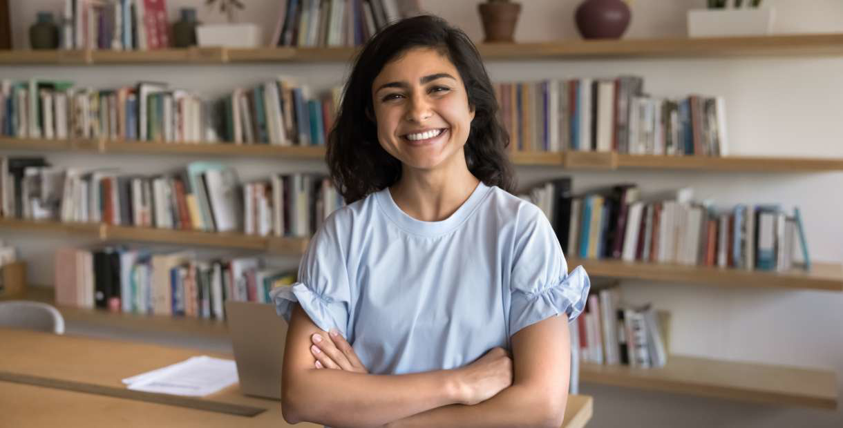 A woman smiling, standing in front of bookshelves.