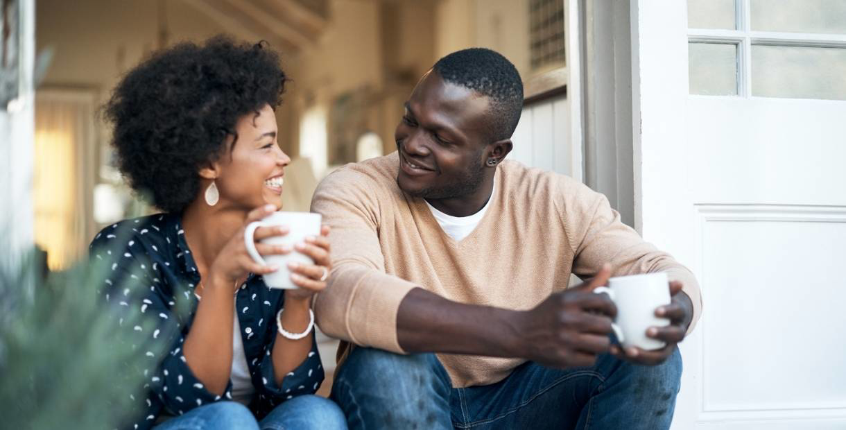 Young couple sitting on the front porch with coffee mugs in their hands.