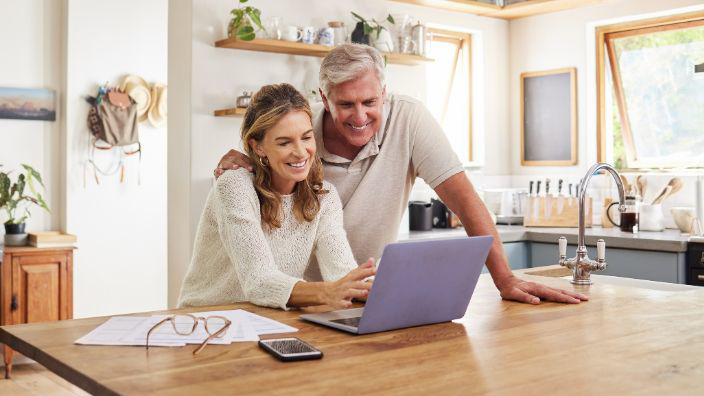 A man and woman sitting at their kitchen counter and looking at their computer together.