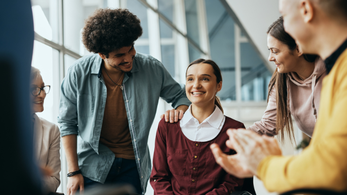 A group of people gathered around a smiling woman and touching her shoulder. 