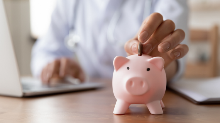 Person in front of their laptop and  putting a coin into piggy bank. 