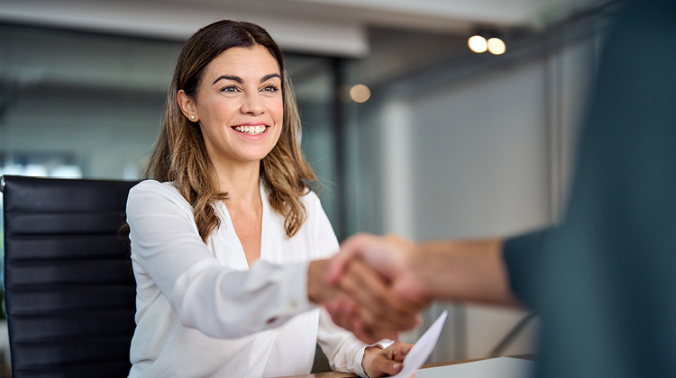 A woman smiles while shaking hands with another person.