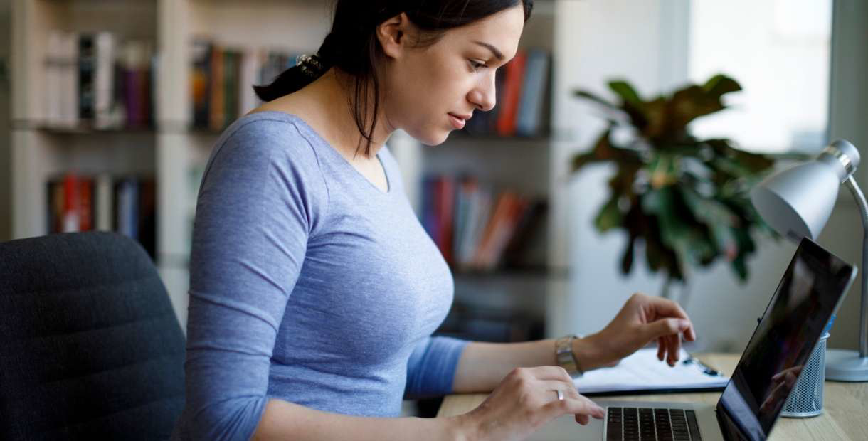 A woman at home on her laptop, looking at the critical illness form.