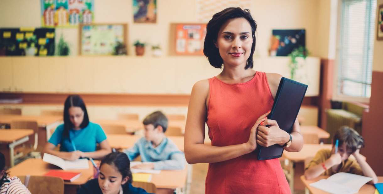 Teacher in classroom with children behind her.