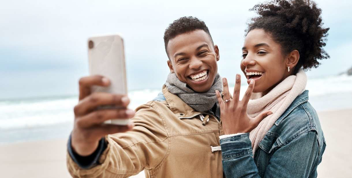 Young engage couple smiling at their mobile phone taking a picture.
