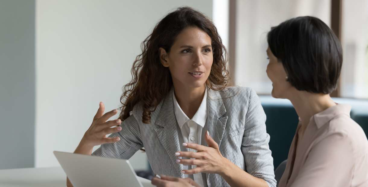 Two people in a professional discussion, seated with a laptop in an office setting.