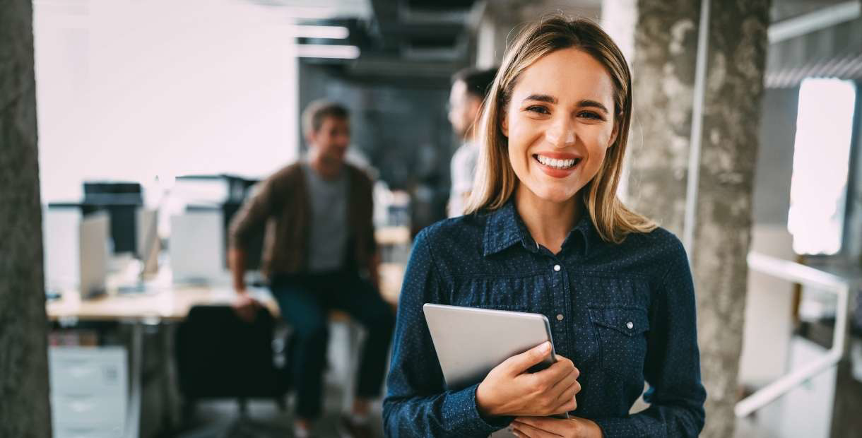 Woman smiling at the camera with an iPad in her hand.