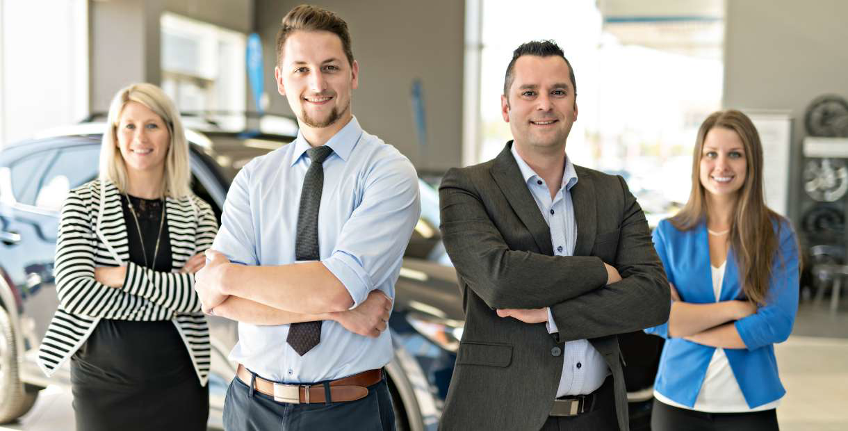 A group of auto business people standing in front of a car.