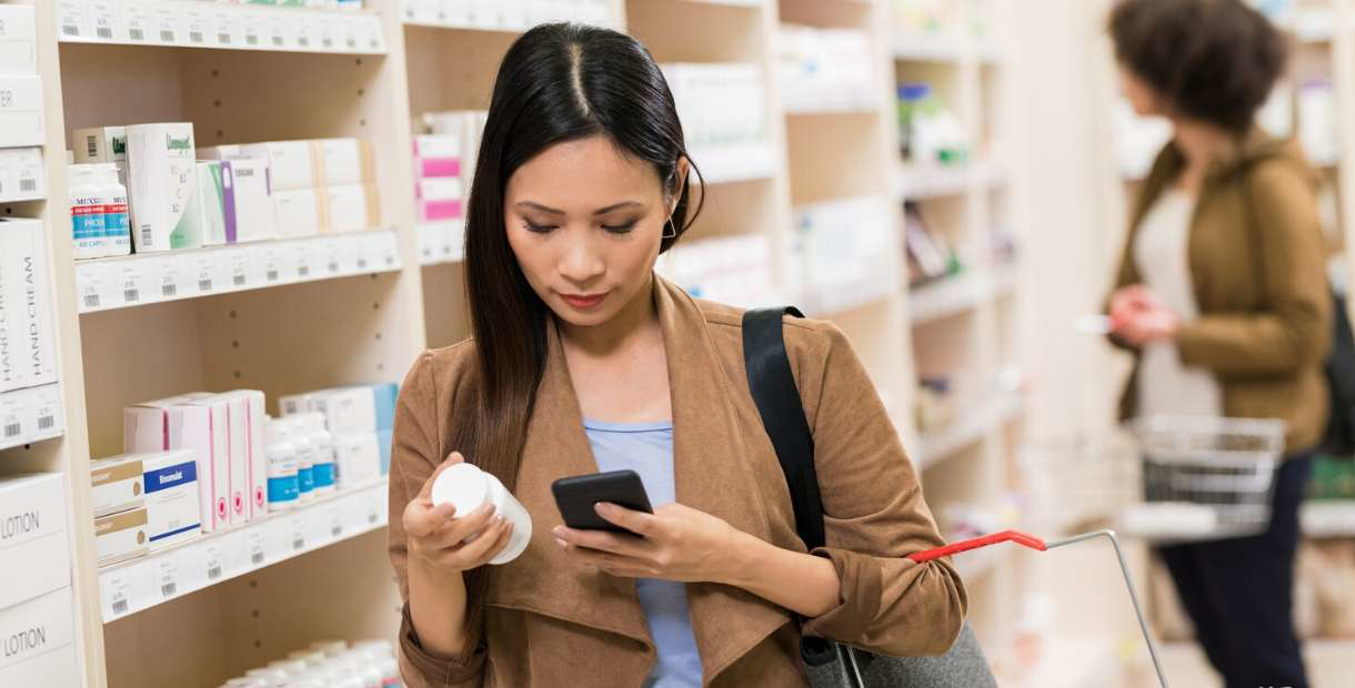 Person comparing medicine in a pharmacy aisle.